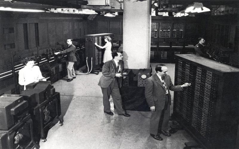 Jean & ENIAC Co-inventors | Group image of several members of the ENIAC team, 1946. Left: ENIAC co-inventors Presper Eckert and Homer Spence.  Center: ENIAC co-inventor John Mauchly. Back Center: Jean Jennings Bartik. Right: Herman Goldstine and Ruth Lichterman (U.S. Army photo from the archives of the ARL Technical Library)